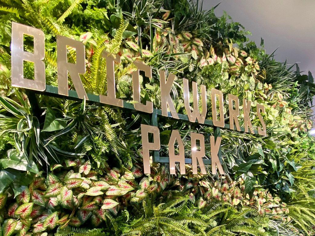 "Brickworks Park" sign on green, leafy wall with gold lettering. The sign is in Brickwork Park's modern sales suite.