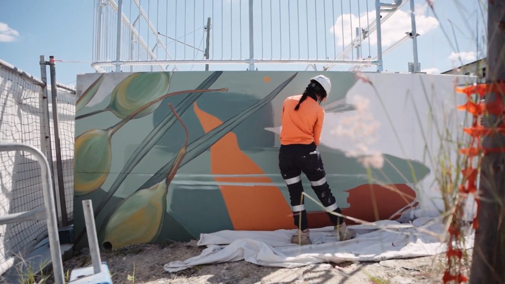 Artist, Ash Taylor painting the mural wearing high vis, helmet and boots. 